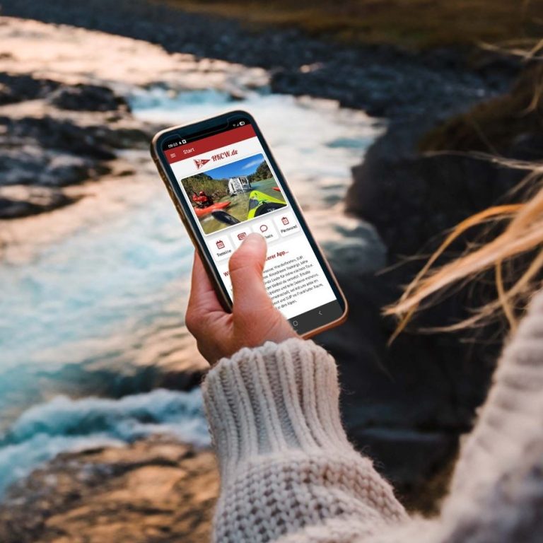 HKCW Vereinsapp Person hält ein Smartphone am Fluss, mit der HKCW-Vereinsapp-Anzeige auf dem Bildschirm.